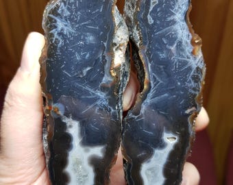 Peut inclure: Deux moitiés d'une géode avec un motif d'agate noir et blanc. La géode a un centre blanc avec des bandes noires autour des bords.