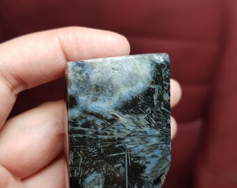 May include: A rectangular, polished stone with a striking pattern of black, white, and blue veining. The stone is held in a hand, showcasing its natural textures and colours. The overall aesthetic suggests a focus on natural materials and unique geological formations.