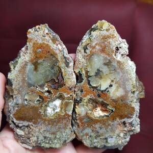 May include: Two halves of a geode, displaying a natural stone formation. The cut surfaces reveal a mix of colours, including brown, orange, and cream, with crystalline structures. The rough edges and varied textures highlight the stone's organic origin.