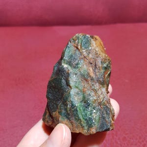 Peut inclure: Une roche brute de couleur verte et brune avec une forme irr&eacute;guli&egrave;re et dentel&eacute;e. La roche a un aspect marbr&eacute; avec des stries vertes et brunes.