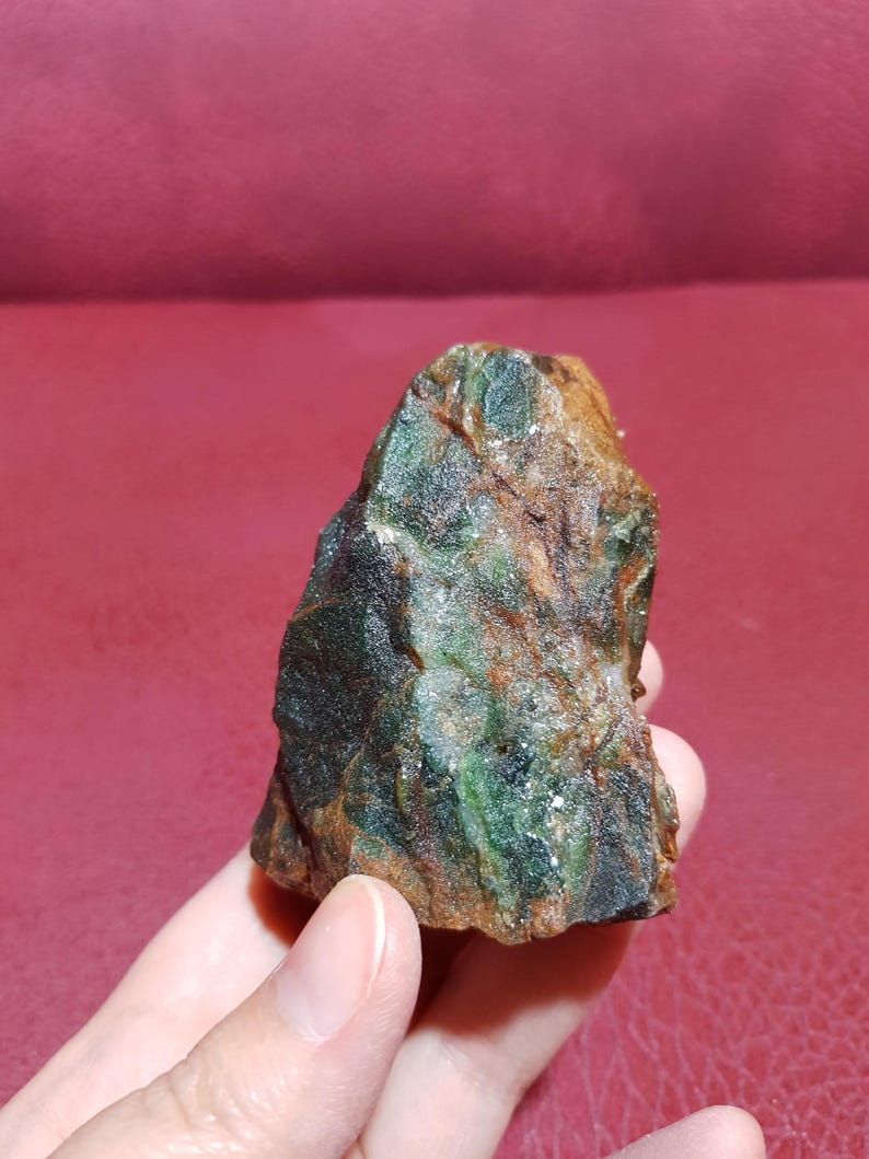 Peut inclure: Une roche brute de couleur verte et brune avec une forme irr&eacute;guli&egrave;re et dentel&eacute;e. La roche a un aspect marbr&eacute; avec des stries vertes et brunes.