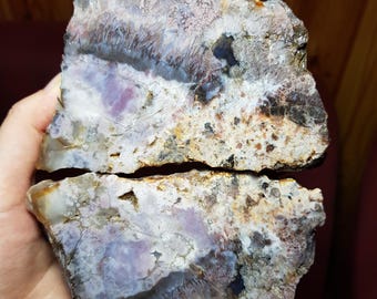 May include: A large, irregularly shaped piece of agate with a purple, white, and brown color scheme. The agate has a layered, banded appearance with a variety of textures.
