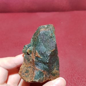 Peut inclure: Une roche brute de couleur verte et brune avec une texture cristalline. La roche a une forme irr&eacute;guli&egrave;re et dentel&eacute;e.