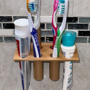 Puede incluir: Un portacepillos de dientes de plástico marrón con cuatro ranuras para cepillos de dientes y un espacio para pasta de dientes. Dos cepillos de dientes azules y blancos, un cepillo de dientes rosa y blanco y un cepillo de dientes verde y blanco están en el portacepillos. Un tubo de pasta de dientes está en el portacepillos.