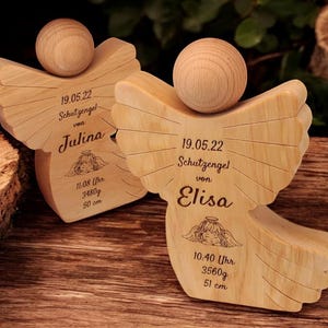 Könnte beinhalten: Zwei Holzengel-Figuren mit gravierten Details. Der erste Engel ist mit "19.05.22 Schutzengel von Julina 11.08 Uhr 3480g 50 cm" beschriftet. Der zweite Engel ist mit "19.05.22 Schutzengel von Elisa 10:40 Uhr 3560g 51 cm" beschriftet.