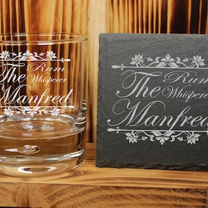 Peut inclure: Un verre en verre transparent avec le texte "The Rum Whisperer Manfred" gravé dessus, à côté d'un dessous-de-verre en ardoise noire avec le même texte.