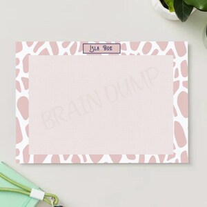 Può includere: Un blocco note rosa e bianco con un bordo di motivo astratto rosa. Il blocco note ha il testo "Isla Boe" in alto.