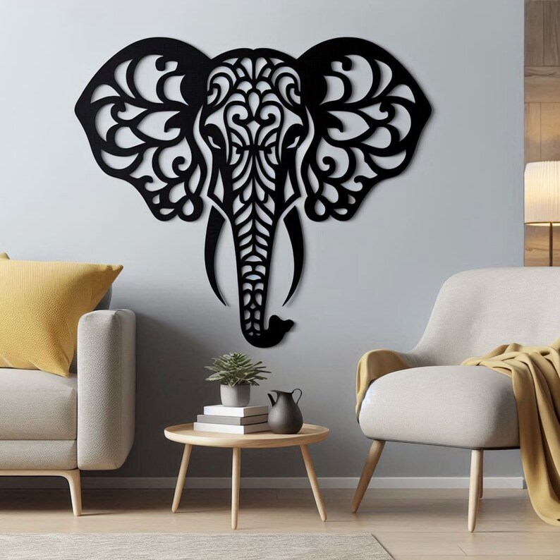 May include: Black silhouette of an elephant's head with intricate floral patterns cut out. The elephant head is mounted on a light gray wall in a living room setting with a couch, chair, and coffee table.