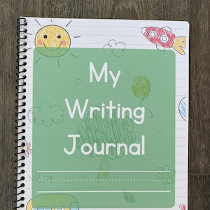 Może przedstawiać: Zielony i biały notes w spirali z napisem "My Writing Journal" na okładce. Okładka zawiera rysunek słońca, rakiety, drzewa, autobusu i kwiatów.