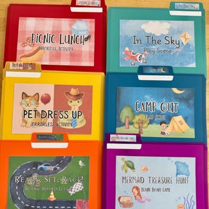 May include: Six colorful file folders featuring educational activity labels: Picnic Lunch, In The Sky, Pet Dress Up, Camp Out, Ready, Set, Race, and Mermaid Treasure Hunt. Each folder displays a thematic illustration and text on a white rectangular insert.