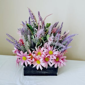 May include: A floral arrangement in a black wooden box. The arrangement features pink daisies and purple lavender.