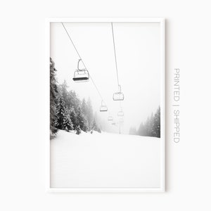 May include: Black and white photograph of a ski lift with empty chairs ascending a snowy mountainside. The lift is surrounded by tall, snow-covered trees.