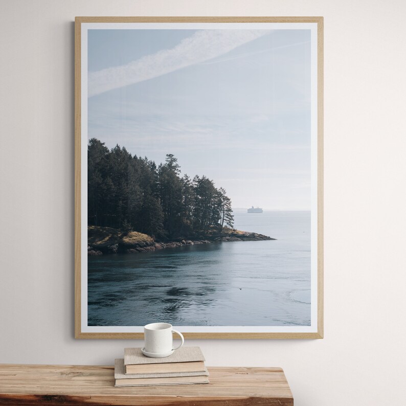 May include: A framed photograph of a forested island with a body of water in the foreground. The water is a deep blue and the sky is a light blue. A small boat is visible in the distance.