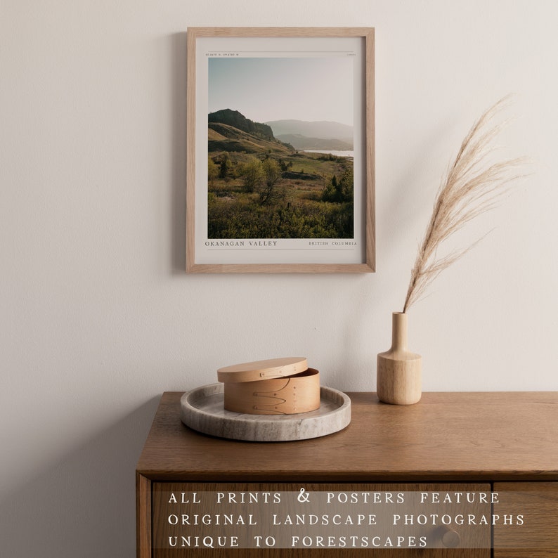 Puede incluir: Una impresi&oacute;n enmarcada de una fotograf&iacute;a de paisaje del valle de Okanagan en Columbia Brit&aacute;nica. La impresi&oacute;n est&aacute; sobre una mesa de madera con un peque&ntilde;o jarr&oacute;n de madera y una caja decorativa.