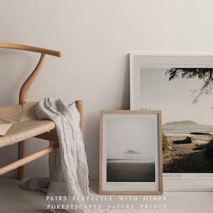 May include: Two framed nature prints with a minimalist aesthetic. The print on the left shows a beach scene with a small island in the distance. The print on the right shows a beach with a tree in the foreground and a mountain in the background. The text on the prints reads "Long Beach" and "ORELINE Vancouver".