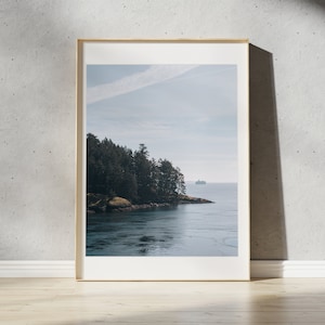May include: A framed photograph of a scenic landscape featuring a body of water with a small island covered in trees in the foreground. The water is a deep blue color and the sky is a light blue with a few white clouds. A small boat is visible in the distance.