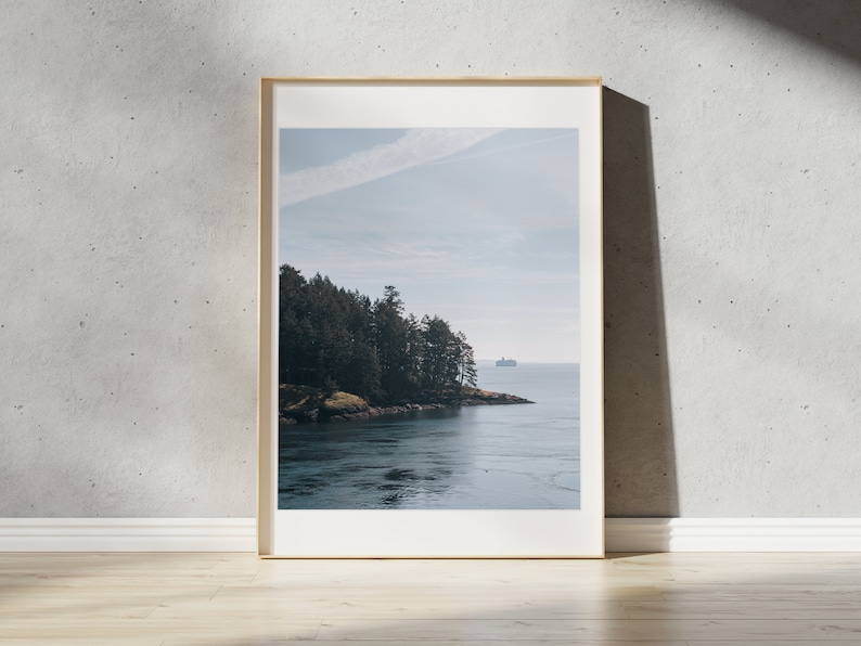 May include: A framed photograph of a scenic landscape featuring a body of water with a small island covered in trees in the foreground. The water is a deep blue color and the sky is a light blue with a few white clouds. A small boat is visible in the distance.