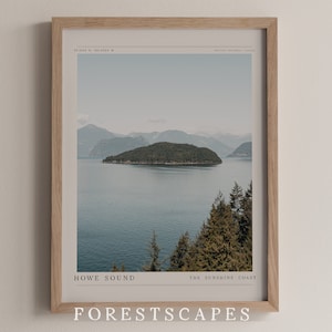 May include: A framed print of a landscape photograph featuring a small island in a body of water with mountains in the background. The text "HOWE SOUND THE SUNSHINE COAST FORESTSCAPES" is printed at the bottom of the image.