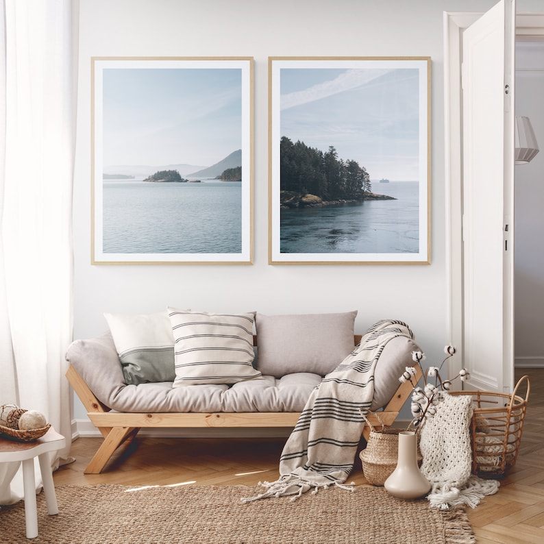 May include: Two framed landscape photographs of a body of water with islands and trees in the distance. The photographs are hanging on a white wall above a wooden futon with a throw blanket and pillows.