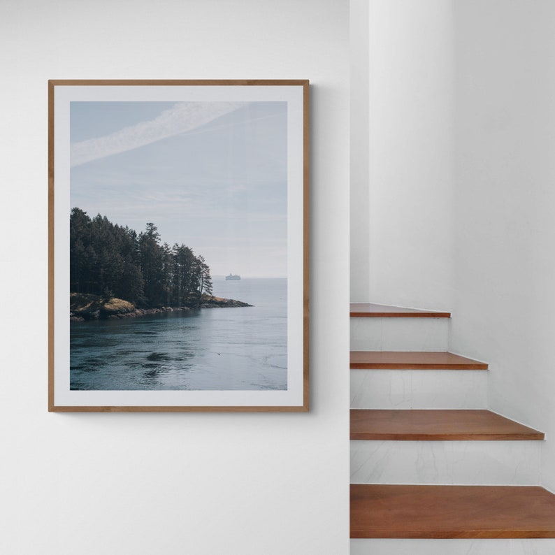 May include: A framed photograph of a forested island with a small boat in the distance, set against a blue sky with white clouds. The water is a deep blue and the island is covered in green trees.