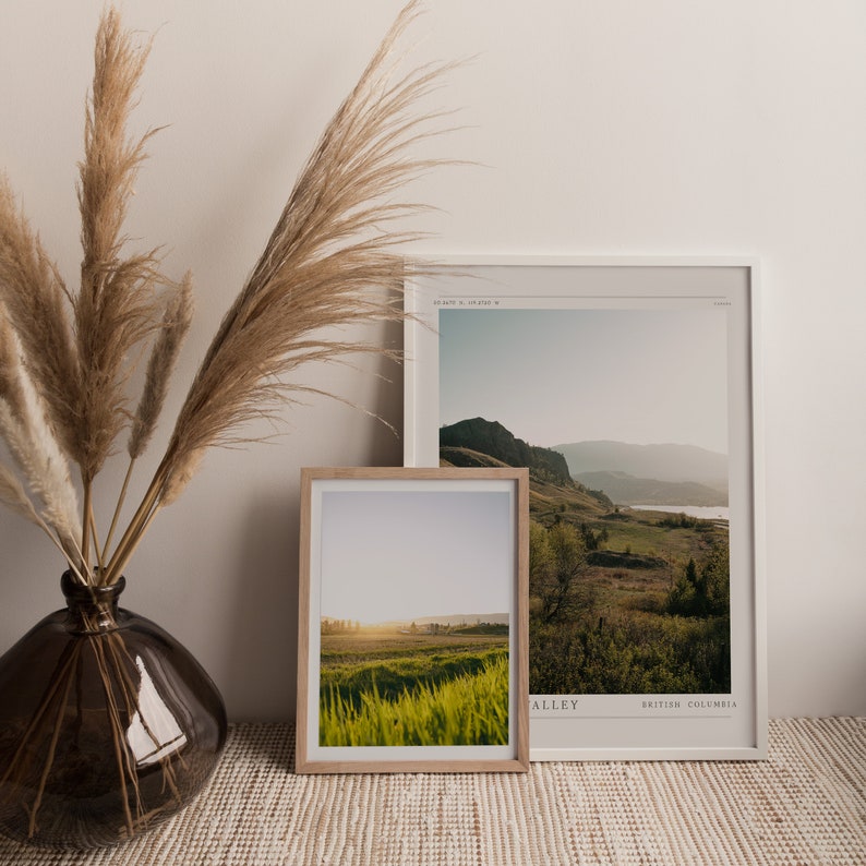 Puede incluir: Dos fotograf&iacute;as de paisajes enmarcadas de un valle verde con monta&ntilde;as en el fondo. La foto superior est&aacute; en un marco blanco y la foto inferior est&aacute; en un marco de madera natural. Ambas fotos est&aacute;n sobre una superficie tejida marr&oacute;n claro.
