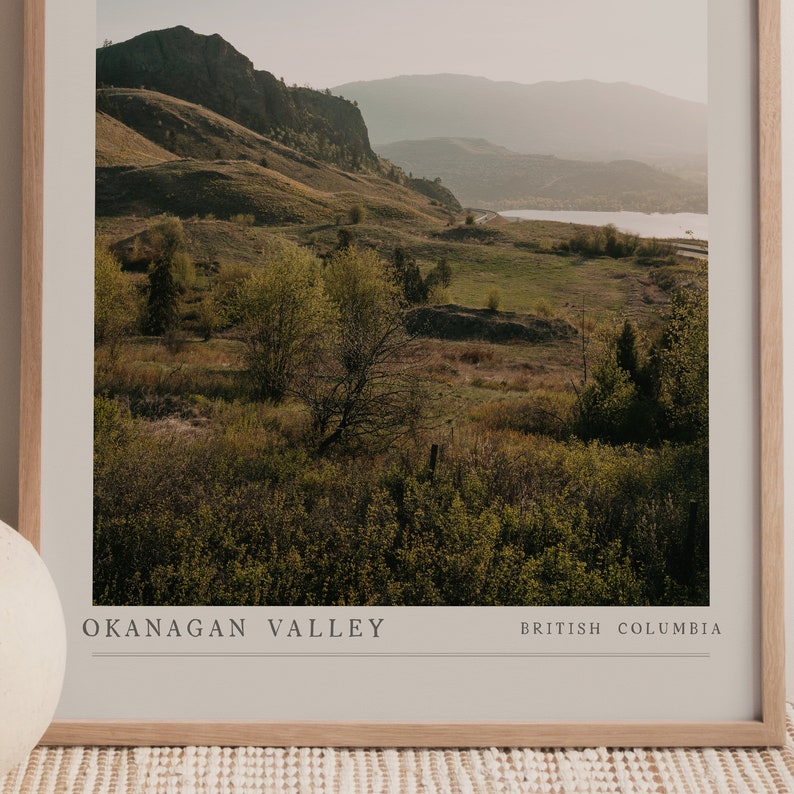 Puede incluir: Una fotograf&iacute;a enmarcada de un paisaje esc&eacute;nico con colinas onduladas, campos verdes y un lago en la distancia. El texto "OKANAGAN VALLEY BRITISH COLUMBIA" est&aacute; impreso en la parte inferior de la imagen.