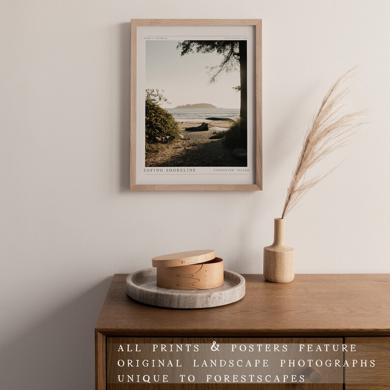 May include: A framed photograph of a beach scene with a wooden frame. The photo shows a sandy beach with a body of water in the background. The text "TOFINO SHORELINE" and "VANCOUVER ISLAND" is printed at the bottom of the photo.