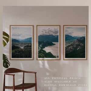 May include: Three framed landscape photographs of a mountain range with a body of water in the foreground. The photos are hung on a white wall with a wooden chair in the foreground.
