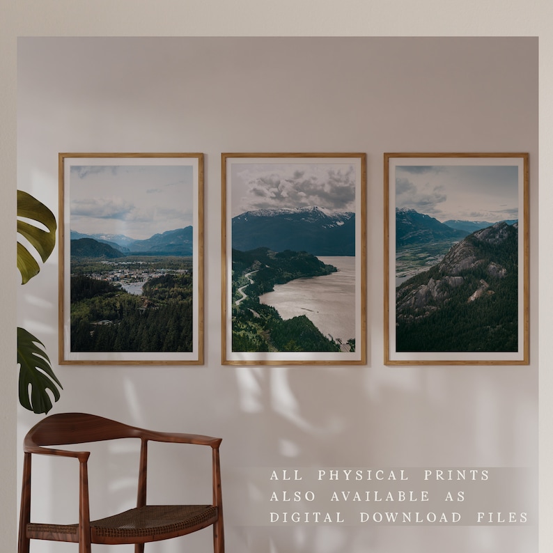 May include: Three framed landscape photographs of a mountain range with a body of water in the foreground. The photos are hung on a white wall with a wooden chair in the foreground.