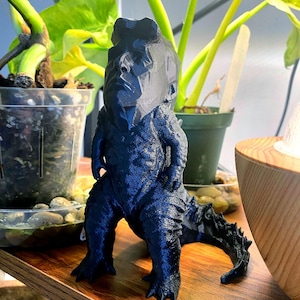Könnte beinhalten: Eine schwarze 3D-gedruckte Figur eines Monsters mit einem menschlichen Kopf. Das Monster steht auf einer Holzoberfläche.