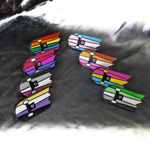 Peut inclure: Huit épingles en émail en forme de planches à roulettes cassées, chacune avec un design de drapeau arc-en-ciel différent. Les drapeaux incluent l'arc-en-ciel, le transgenre, le bisexuel, le genderqueer, le pansexuel, lesbien, asexuel et non-binaire.