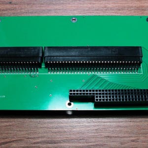 May include: A green circuit board with multiple black connectors and pins. The board has a rectangular shape with rounded corners and several mounting holes. The surface has traces and text.