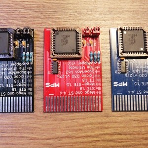 Puede incluir: Tres placas de circuito con componentes electrónicos se muestran sobre una superficie de madera. Las placas son negras, rojas y azules, cada una con una disposición diferente de chips, resistencias y conectores. El texto en las placas incluye "Mega and ST 4.4" y "STE 1.9".