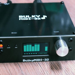 Könnte beinhalten: Schwarzer Bulky MIDI-32 Synthesizer mit grünem Grafik-Equalizer-Display. Er hat einen silbernen Knopf und Tasten mit der Aufschrift "Power", "Synth" und "ROM". Der Text "Bulky MIDI-32" ist auf der Vorderseite aufgedruckt.