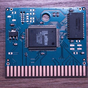Könnte beinhalten: Eine türkisfarbene Leiterplatte mit verschiedenen elektronischen Bauteilen, darunter ein zentraler Prozessor mit der Aufschrift "Lattice" und ein rechteckiger Chip. Die Platine hat eine Reihe goldfarbener Stifte entlang der Unterkante. Der Hintergrund ist eine dunkle Holzoberfläche.