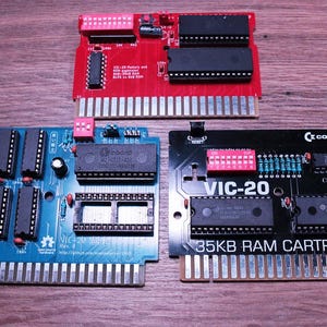 Pode incluir: Três placas de circuito de computador vintage em vermelho, azul e preto. A placa vermelha tem o texto "VIC-20 Memory and ROM Expansion". A placa azul tem o texto "VIC-20 Super". A placa preta está rotulada como "VIC-20 35KB RAM CARTRIDGE".