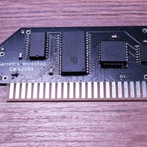 May include: A black circuit board with multiple integrated circuits and a gold-colored connector. The text "Garrett's Workshop GW 4208A" is printed on the board. The board is set against a wooden surface.