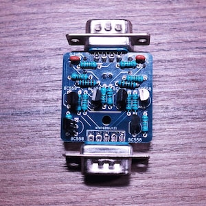 May include: A blue circuit board featuring electronic components, such as resistors and capacitors, connected to two silver connectors. The board is marked with "BC558". The background is a wooden surface.