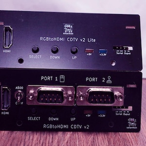 May include: Two black electronic devices stacked on top of each other. The top device is labeled "RGBtoHDMI CDTV v2 Lite" and has HDMI and other ports. The bottom device is labeled "RGBtoHDMI CDTV v2" and has multiple ports including HDMI and A500.