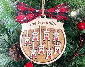 May include: A wooden Christmas ornament shaped like a reindeer with a red and black plaid bow. The ornament is personalized with the text "The G Family" and the names of family members: Mom, Zander, Jaelyn, Dad, JJ, Naomi, Frankie Jr., and Komasan.
