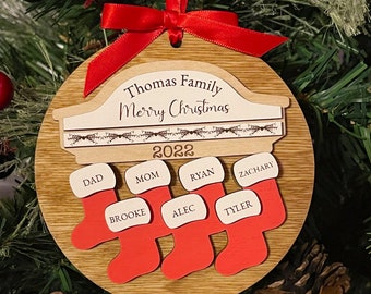 May include: A wooden Christmas ornament with the text "Thomas Family Merry Christmas 2022" and six red stockings with names written on them.