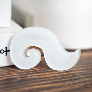 May include: A translucent white, swirl-shaped decorative object. The object has a smooth, curved design with a central opening. It rests on a dark wood surface, with a blurred white background.