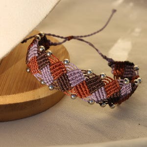 May include: A purple, brown, and orange braided bracelet with silver beads.