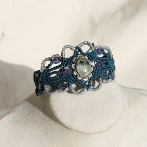 May include: A teal and silver macrame bracelet with a green gemstone and purple beads.