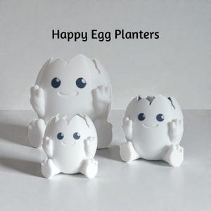 Puede incluir: Tres macetas blancas en forma de huevo con caras sonrientes, brazos y piernas. Las macetas tienen una parte superior agrietada, y el texto "Happy Egg Planters" está encima.