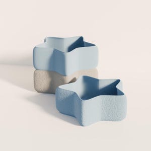 May include: Three star-shaped containers in a light blue colour. One container is stacked on a beige textured block, with another container placed in front. The containers have a textured surface and a unique, modern design.