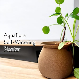 Puede incluir: Una maceta auto-riego marrón con una planta verde en su interior. La maceta está etiquetada como "Aquaflora Self-Watering Planter".