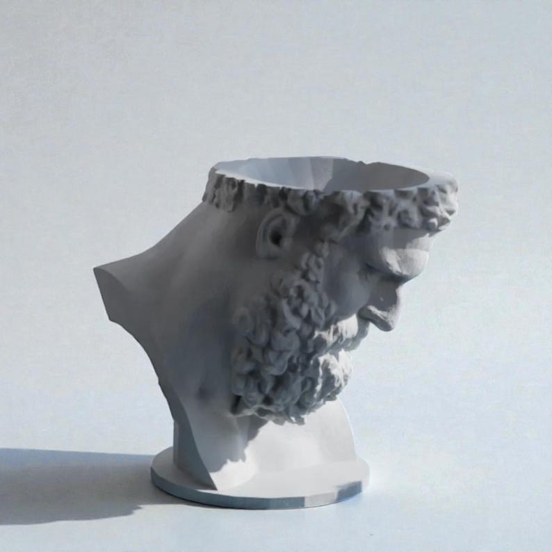May include: A matte white sculptural planter shaped like a classical bust of a bearded figure with a hollowed-out top. The head is tilted downward, featuring detailed curls in the hair and beard, resting on a circular base with a smooth finish.
