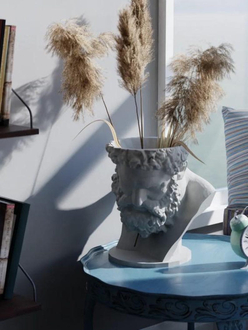 May include: A white sculptural vase shaped like a bearded male head, featuring detailed facial features and hair. The hollow top of the head holds three tall, feathery, light brown dried pampas grass stems, creating a textured and natural display.