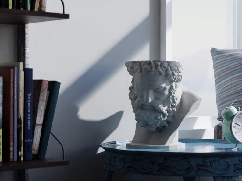 May include: A light gray sculptural planter shaped like the head of a bearded man with curly hair. The hollow bust features detailed facial features including a prominent brow, deep-set eyes, and a thick beard, serving as a decorative container.